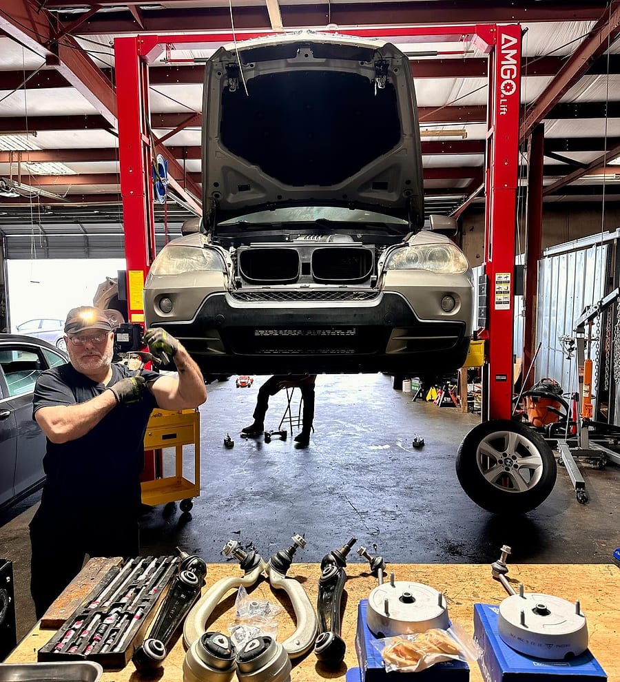 HTL technician in front of a BMW X5 on the lift, with new suspension parts on the bench